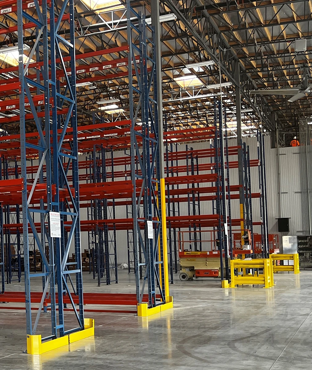 Yellow end-of-row pallet rack guardrails and bollards installed in warehouse during pallet rack installation